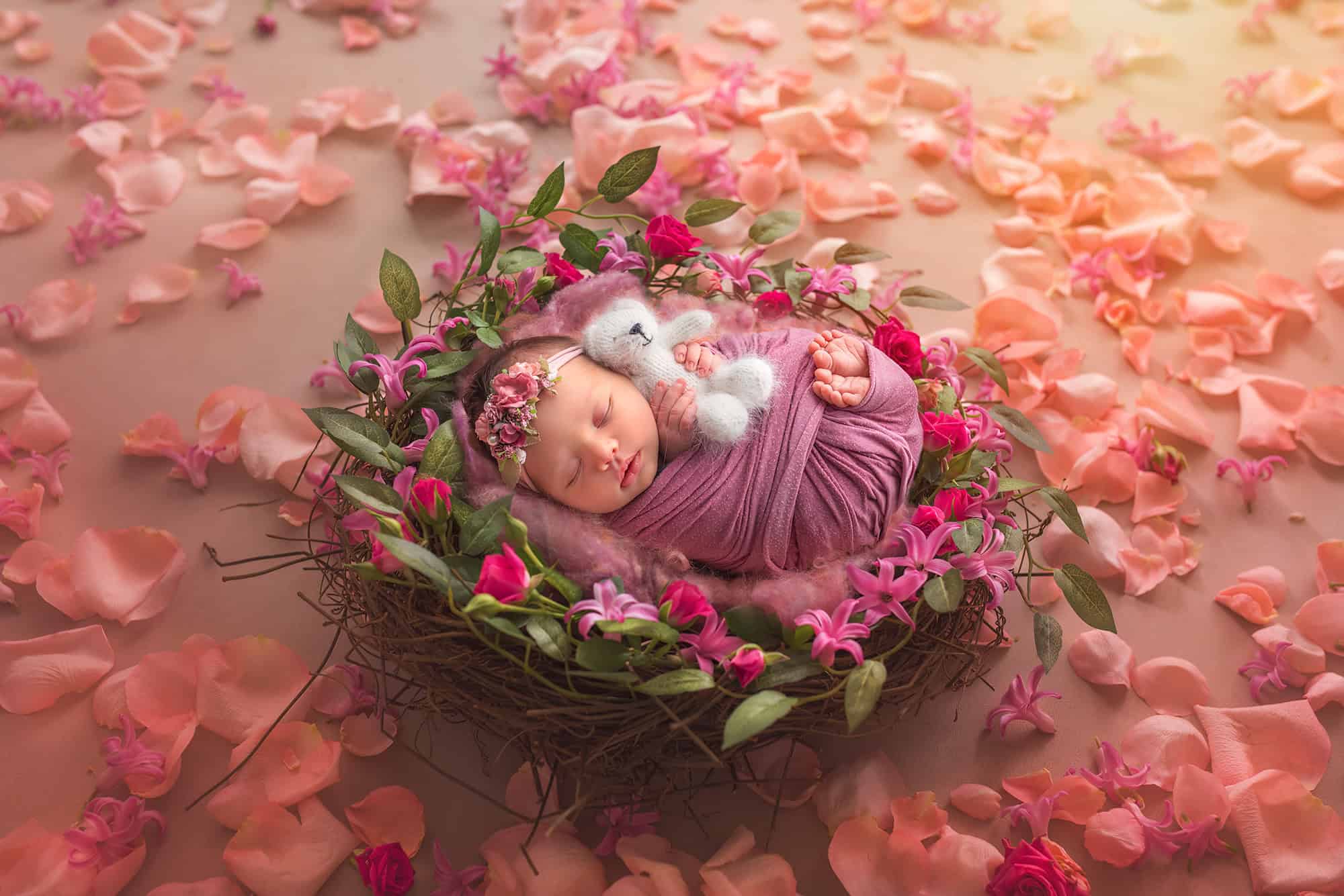 maternity and newborn photography Brooklyn in a nest surrounded by flowers, holding a white teddy bear.
