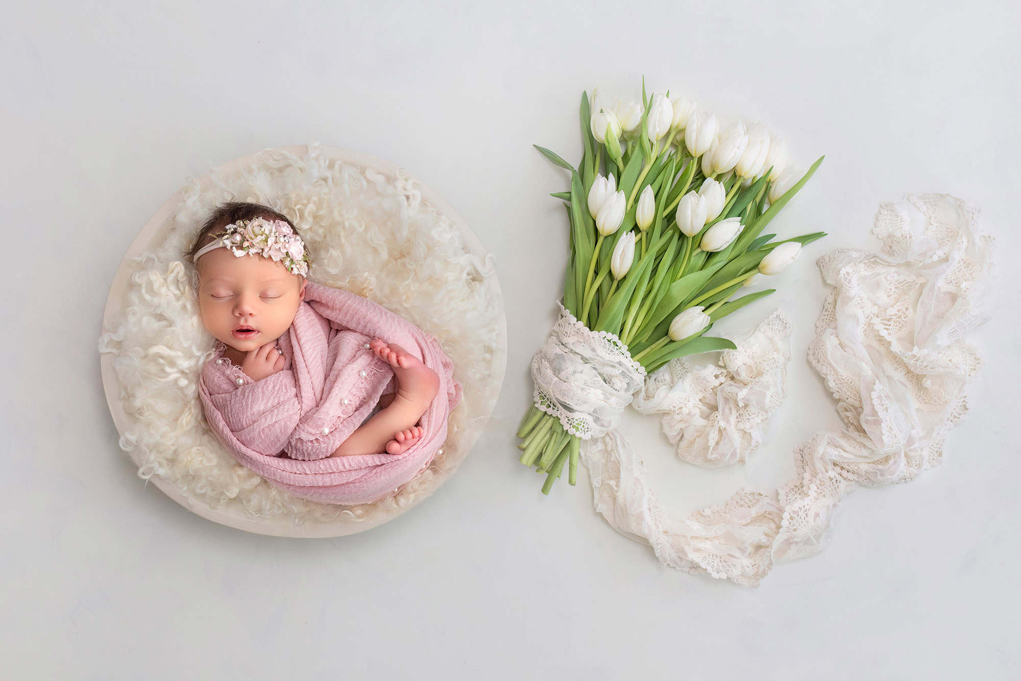 Brooklyn in a white bowl with a bouquet of white tulips lying next to her.