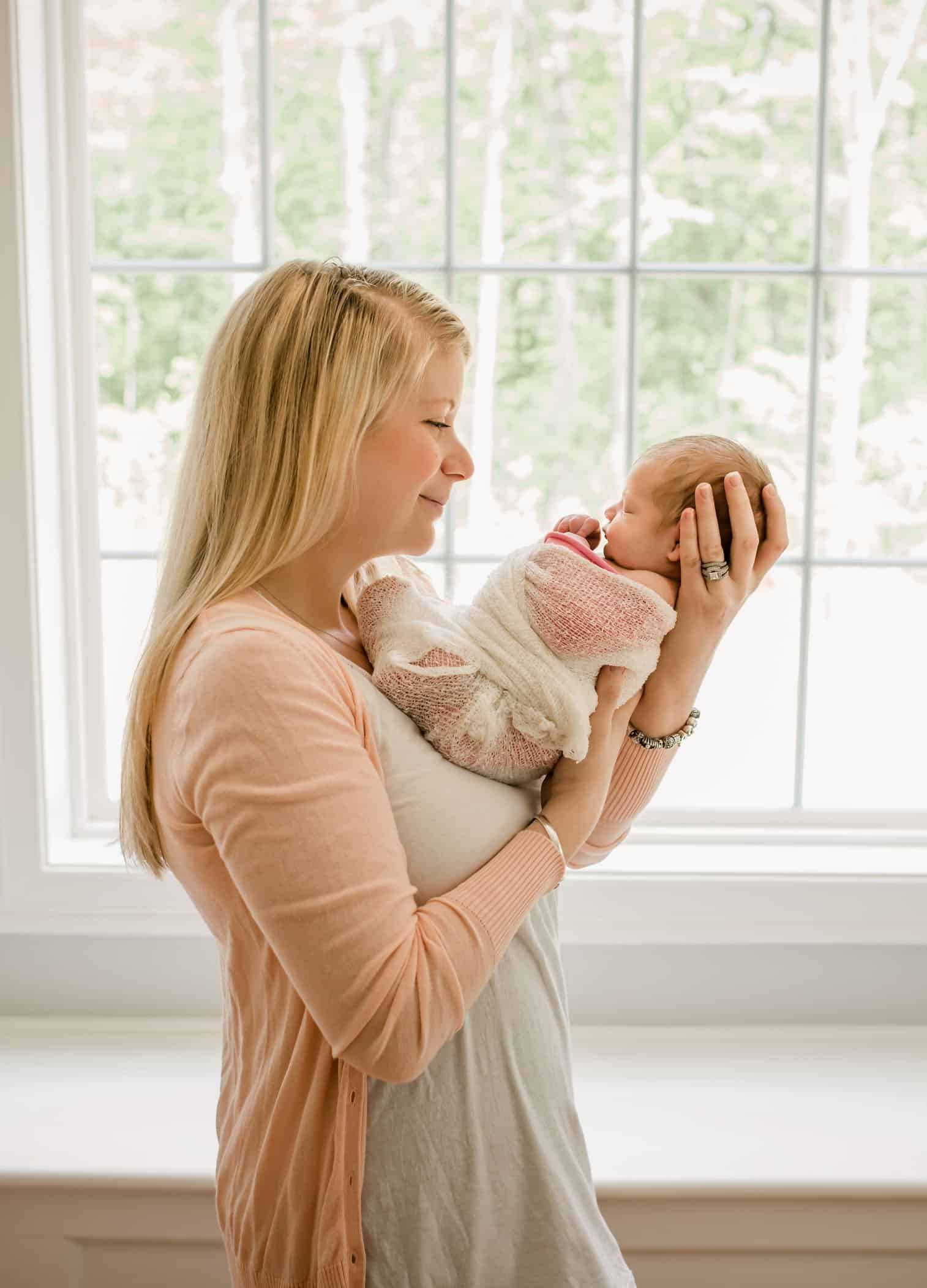 Mom looking at baby on her chest in front of big picture window