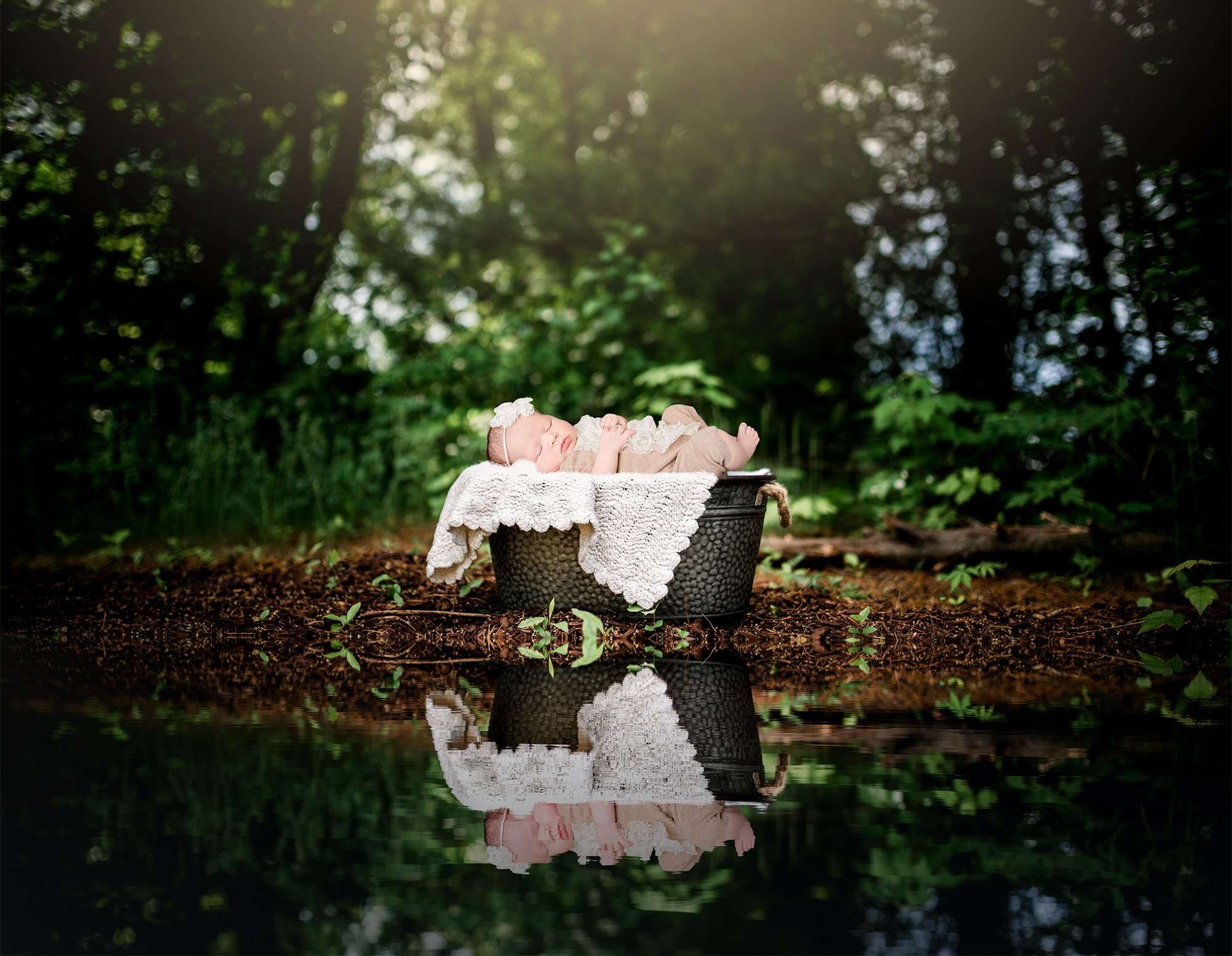 newborn baby sleeping in a bucket in the woods by a pond One Big Happy Photo