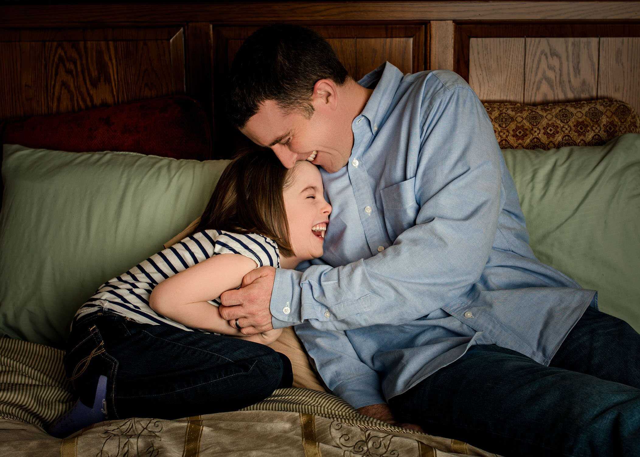 Daddy laughing with 5 year old daughter on bed