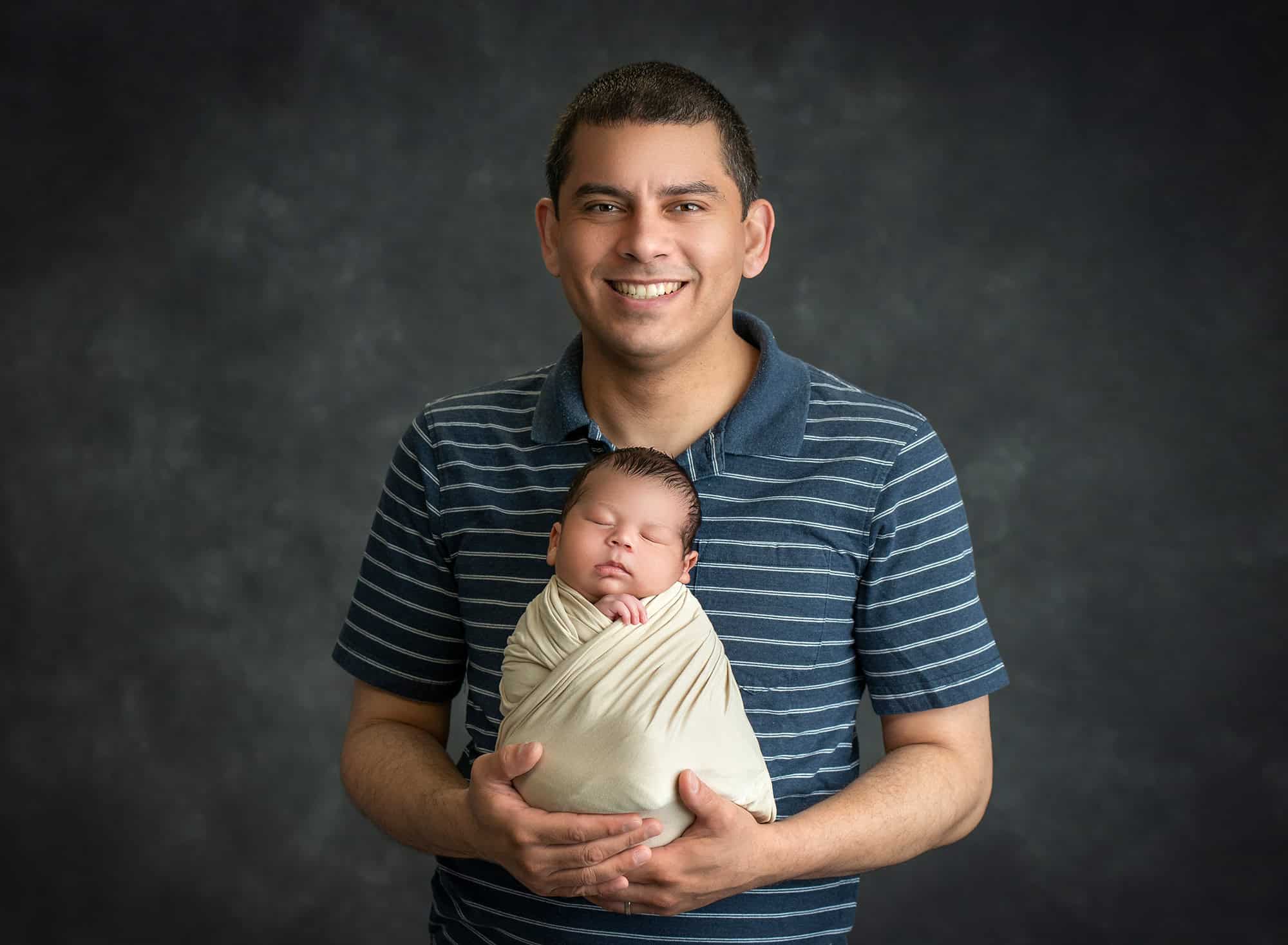 dad cradling newborn baby boy swaddled in cream