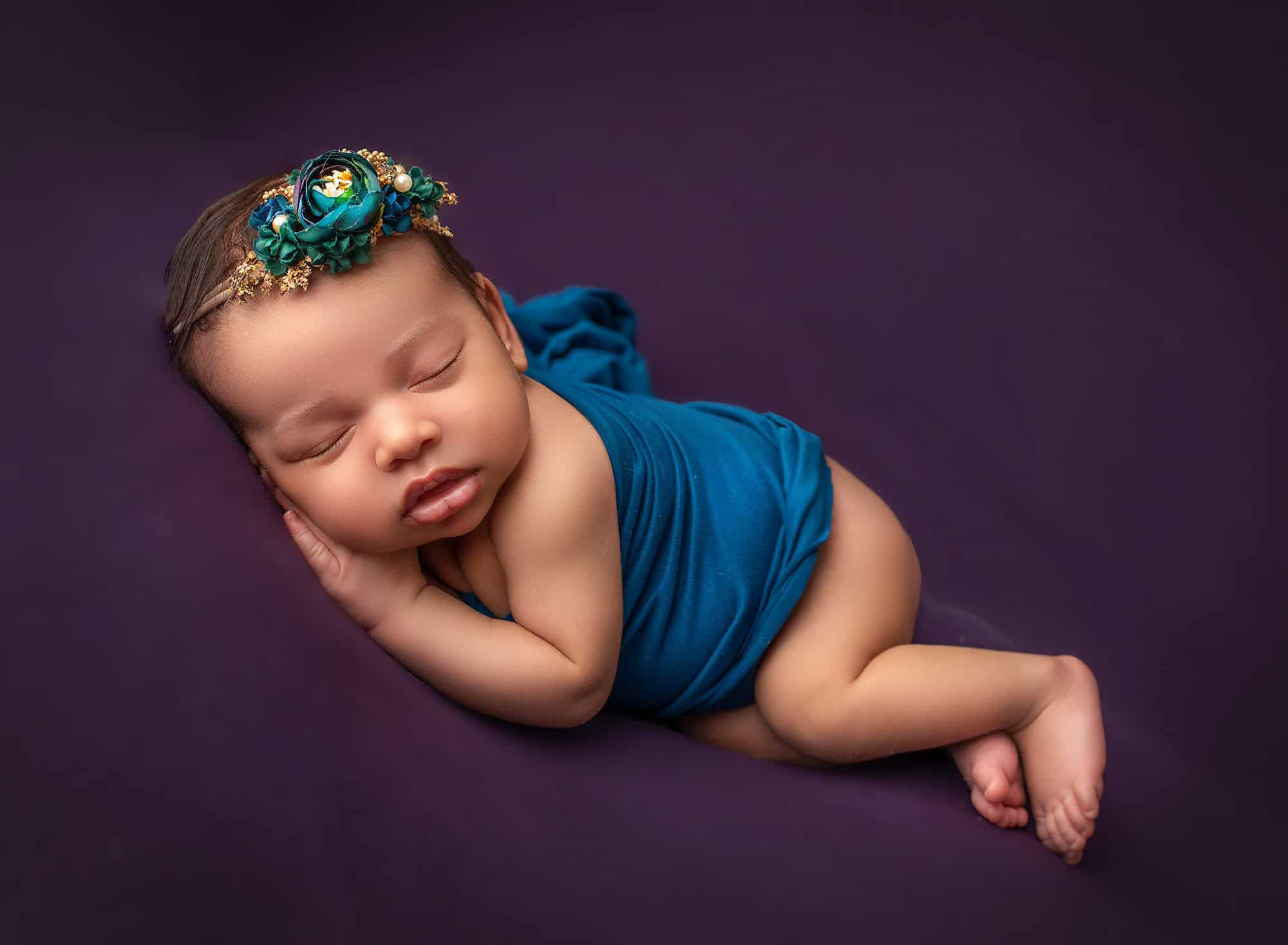 how to prepare for newborn photoshoot Glastonbury CT newborn photoshoot newborn baby girl asleep on a background of purple dressed in a teal wrap and floral headband