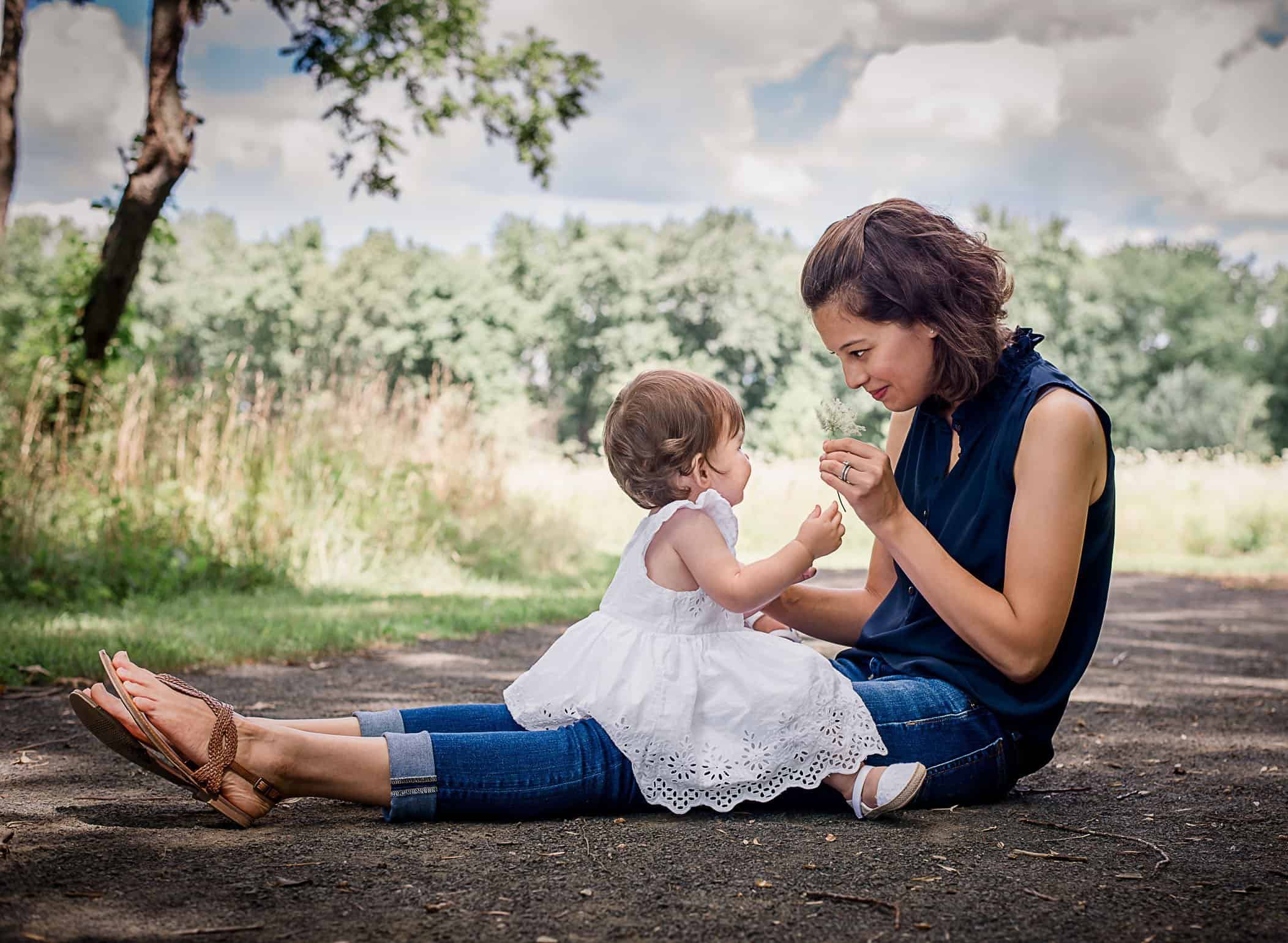one year old baby girl picture sitting on Mama's lap playing with a flower One Big Happy Photo