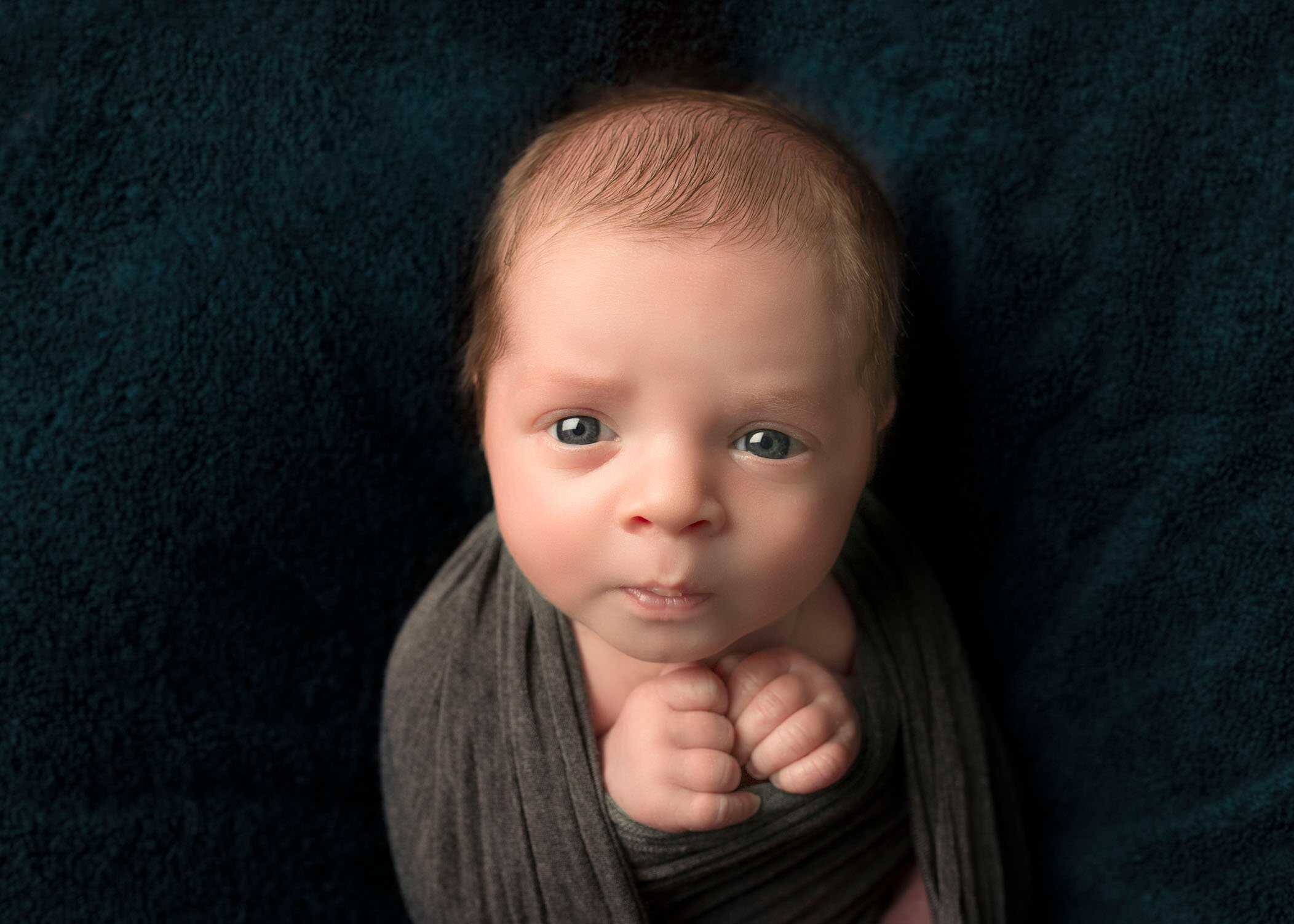newborn boy looking at camera hands together